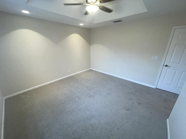 spare room with a tray ceiling, ceiling fan, and dark colored carpet