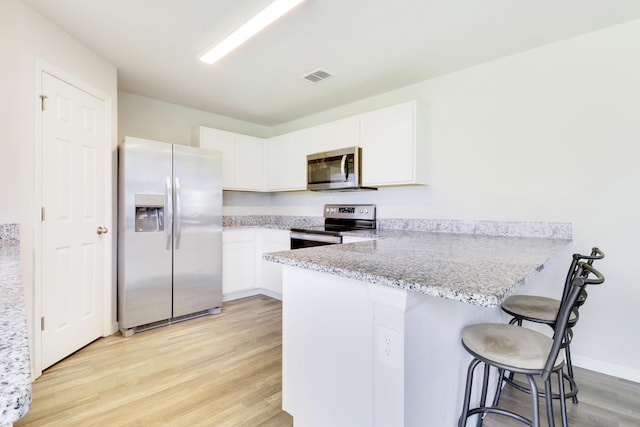 kitchen featuring a kitchen breakfast bar, kitchen peninsula, white cabinetry, and appliances with stainless steel finishes