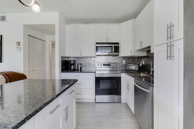 kitchen featuring sink, appliances with stainless steel finishes, white cabinets, decorative backsplash, and dark stone counters