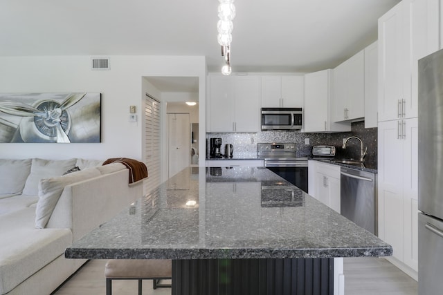 kitchen featuring white cabinetry, appliances with stainless steel finishes, a center island, and dark stone counters