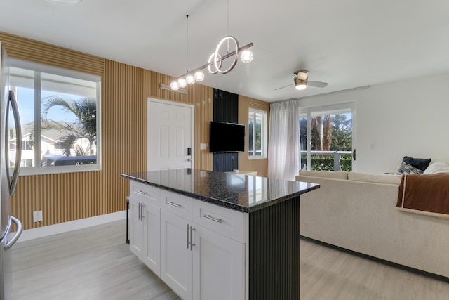 kitchen with white cabinetry, a center island, light hardwood / wood-style floors, decorative light fixtures, and dark stone counters