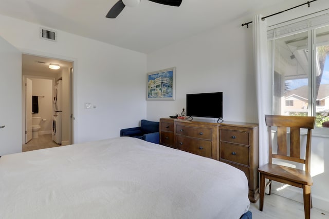 bedroom featuring ensuite bathroom, stacked washing maching and dryer, ceiling fan, and light hardwood / wood-style flooring