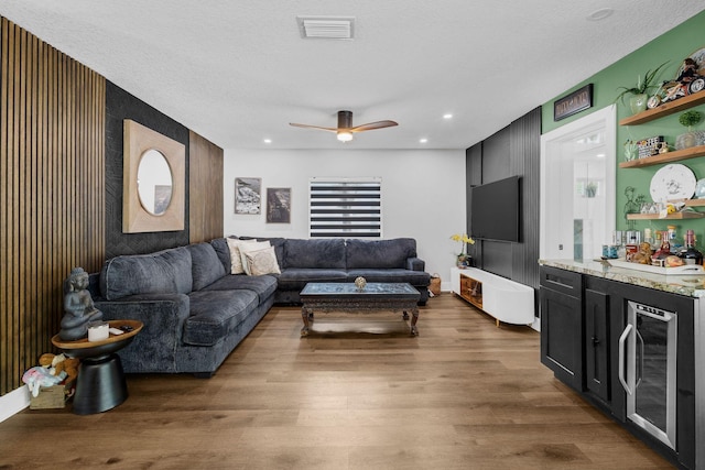 living room with a textured ceiling, bar, wine cooler, dark hardwood / wood-style flooring, and ceiling fan