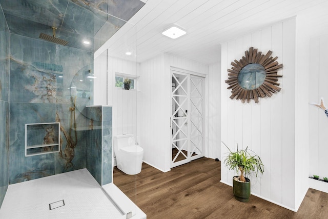 bathroom featuring toilet, wooden walls, tiled shower, and hardwood / wood-style floors