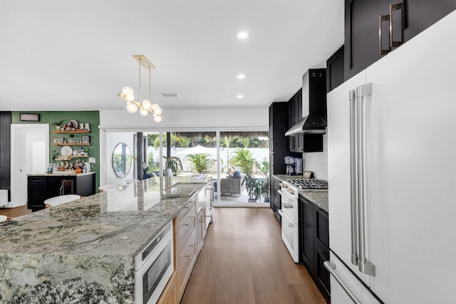 kitchen with stainless steel microwave, wall chimney exhaust hood, double oven range, hanging light fixtures, and high end fridge