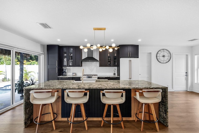 kitchen with wall chimney range hood, a kitchen island with sink, a kitchen bar, and premium appliances