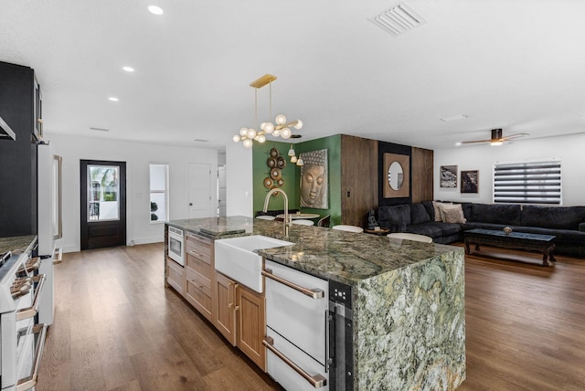 kitchen featuring a center island with sink, hanging light fixtures, dark stone counters, stainless steel microwave, and sink