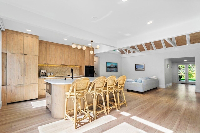 kitchen featuring hanging light fixtures, tasteful backsplash, vaulted ceiling with beams, an island with sink, and a breakfast bar area