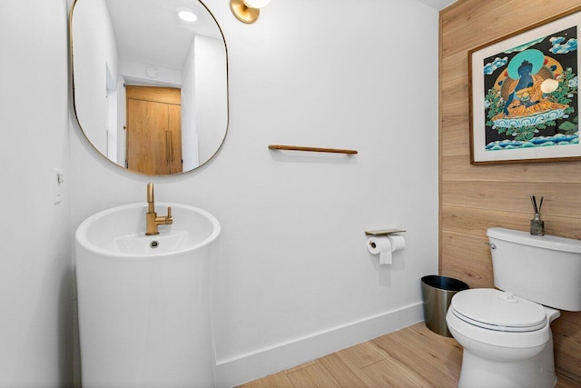 bathroom with wood walls, hardwood / wood-style floors, sink, and toilet