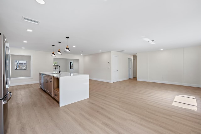 kitchen featuring sink, decorative light fixtures, a center island with sink, stainless steel appliances, and light hardwood / wood-style floors