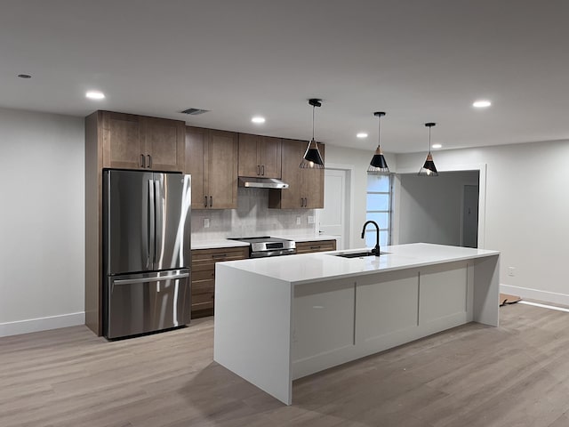 kitchen featuring light hardwood / wood-style floors, hanging light fixtures, sink, an island with sink, and stainless steel appliances