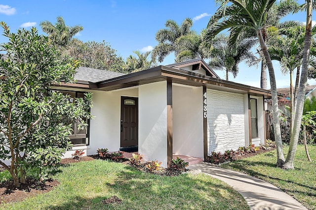 view of front of property with stucco siding, a front lawn, and roof with shingles