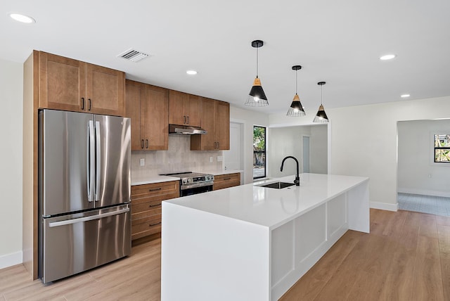 kitchen with sink, tasteful backsplash, a center island with sink, light hardwood / wood-style flooring, and appliances with stainless steel finishes