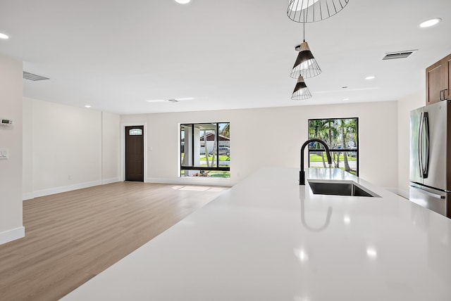 kitchen with a healthy amount of sunlight, sink, stainless steel refrigerator, and light hardwood / wood-style floors