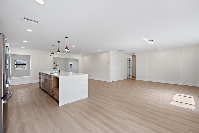 kitchen with appliances with stainless steel finishes, pendant lighting, sink, a large island, and light wood-type flooring