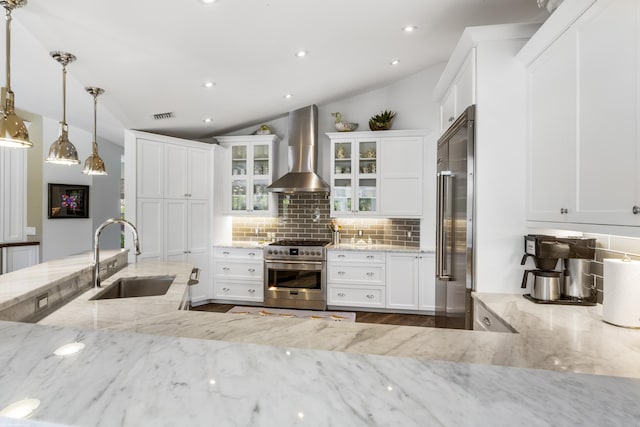 kitchen featuring wall chimney range hood, sink, hanging light fixtures, vaulted ceiling, and premium appliances