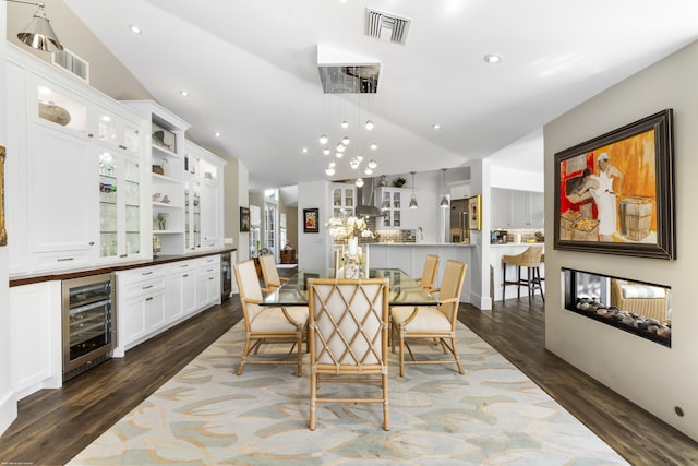 dining room with a multi sided fireplace, vaulted ceiling, wine cooler, and dark wood-type flooring