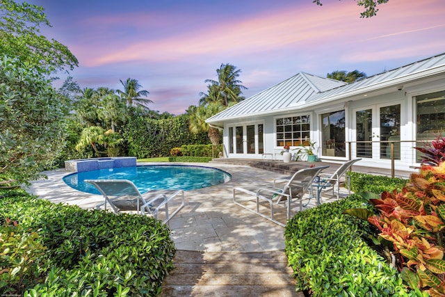 pool at dusk with french doors and a patio area