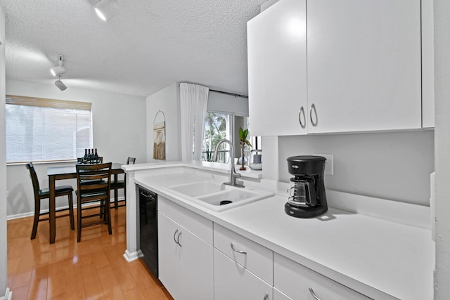 kitchen featuring dishwasher, light wood-type flooring, light countertops, white cabinets, and a sink