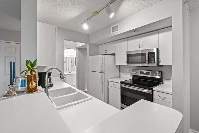 kitchen featuring sink, rail lighting, appliances with stainless steel finishes, white cabinetry, and a textured ceiling