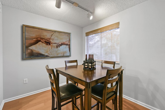 dining area featuring rail lighting, wood finished floors, baseboards, and a textured ceiling