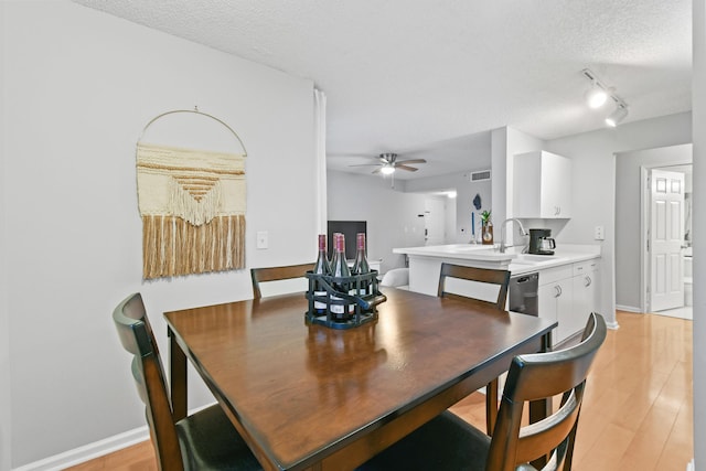 dining room featuring baseboards, visible vents, light wood finished floors, ceiling fan, and a textured ceiling