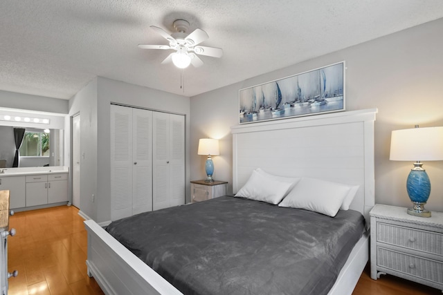 bedroom featuring ensuite bathroom, a ceiling fan, a textured ceiling, wood finished floors, and a closet