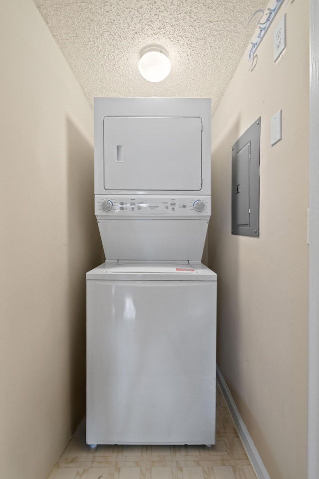 laundry area featuring baseboards, light floors, electric panel, stacked washer and clothes dryer, and a textured ceiling