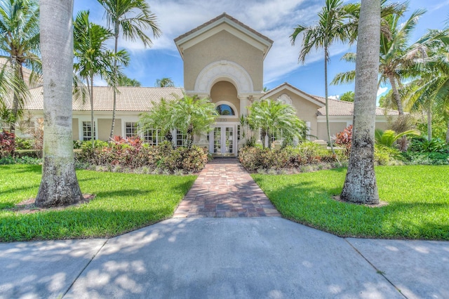 mediterranean / spanish home with a tiled roof, stucco siding, french doors, and a front lawn