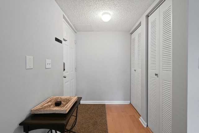 hall featuring light wood-style flooring, baseboards, and a textured ceiling