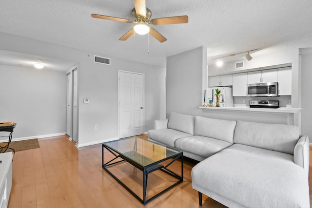 living area with a textured ceiling, visible vents, and ceiling fan