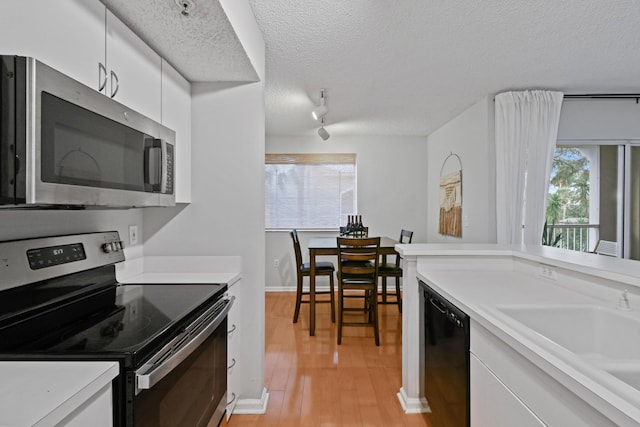 kitchen with a sink, a textured ceiling, appliances with stainless steel finishes, white cabinets, and light countertops