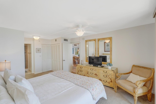 bedroom with ceiling fan, light colored carpet, and two closets