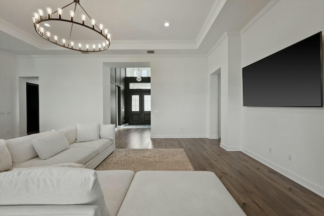 living room featuring dark wood-type flooring, crown molding, a tray ceiling, and a notable chandelier