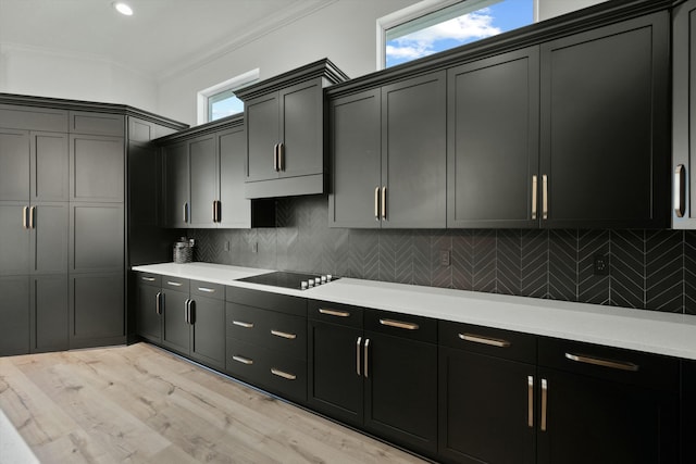 kitchen with a healthy amount of sunlight, black electric stovetop, crown molding, tasteful backsplash, and light hardwood / wood-style floors