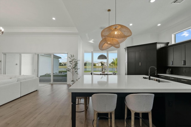 kitchen with a center island with sink, crown molding, sink, tasteful backsplash, and decorative light fixtures