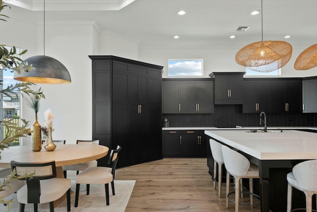 kitchen with backsplash, sink, light hardwood / wood-style flooring, ornamental molding, and decorative light fixtures