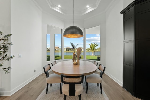 dining area featuring a raised ceiling, a water view, ornamental molding, and light wood-type flooring