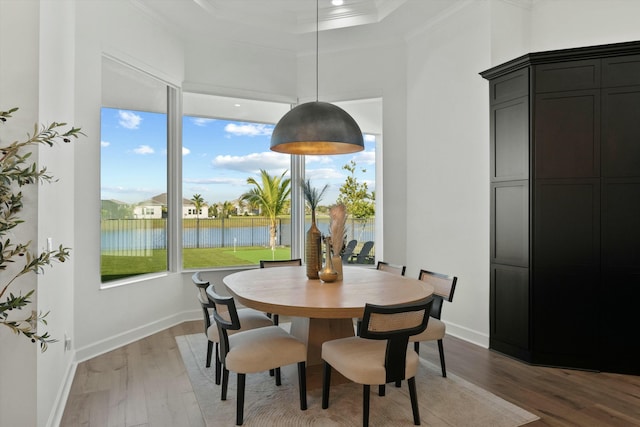 dining space with a water view, ornamental molding, and wood-type flooring