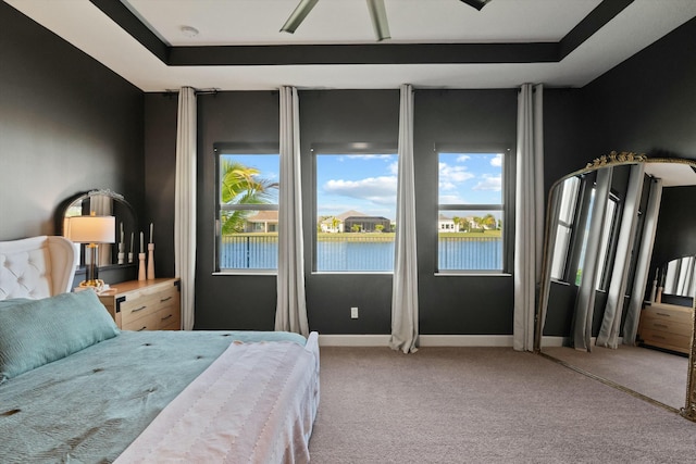 bedroom with carpet floors, a water view, ceiling fan, and a tray ceiling