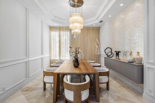 dining space featuring a raised ceiling, ornamental molding, and a chandelier