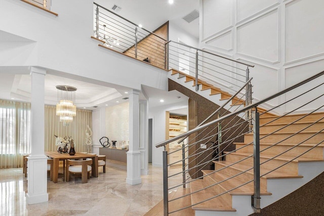 stairs with a raised ceiling, a towering ceiling, an inviting chandelier, and ornate columns