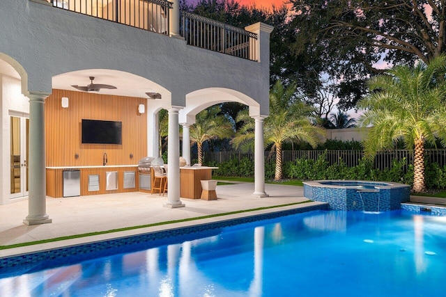 pool at dusk featuring an in ground hot tub, area for grilling, exterior bar, ceiling fan, and a patio area