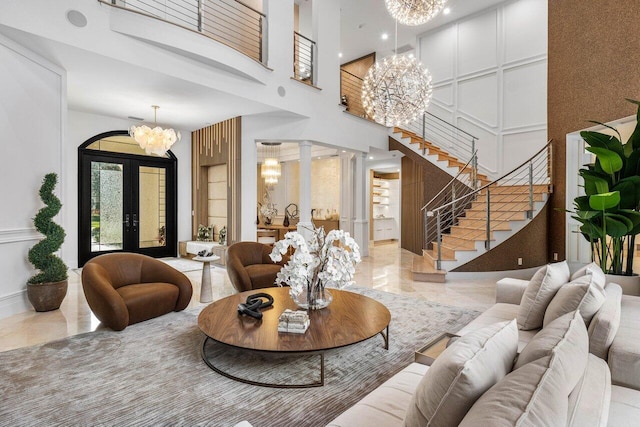 living room with french doors, a towering ceiling, decorative columns, and a notable chandelier