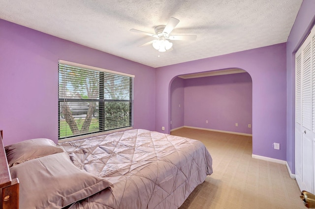 bedroom featuring light carpet, a closet, ceiling fan, and a textured ceiling