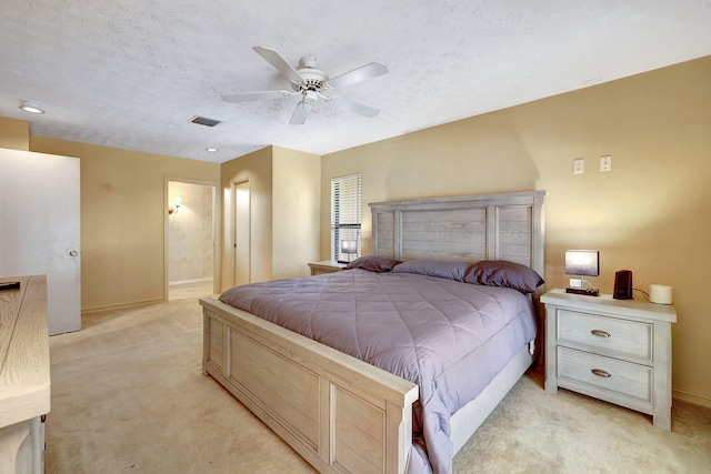 bedroom with ceiling fan, light colored carpet, ensuite bathroom, and a textured ceiling