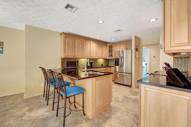 kitchen featuring stainless steel appliances, sink, light brown cabinets, tasteful backsplash, and kitchen peninsula