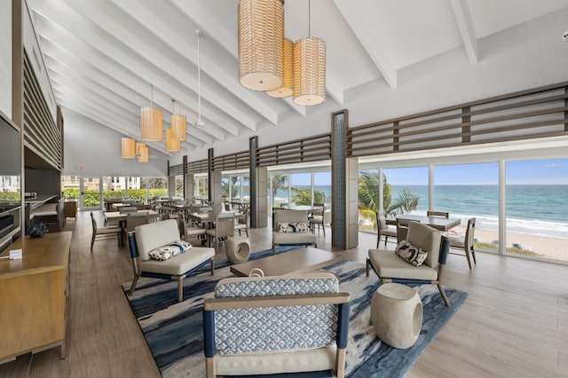 living room with a high ceiling, beamed ceiling, hardwood / wood-style floors, a view of the beach, and a water view