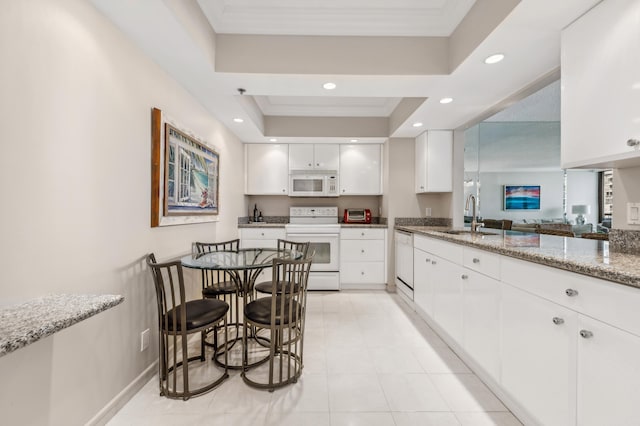 kitchen with light stone countertops, white appliances, a raised ceiling, sink, and white cabinets