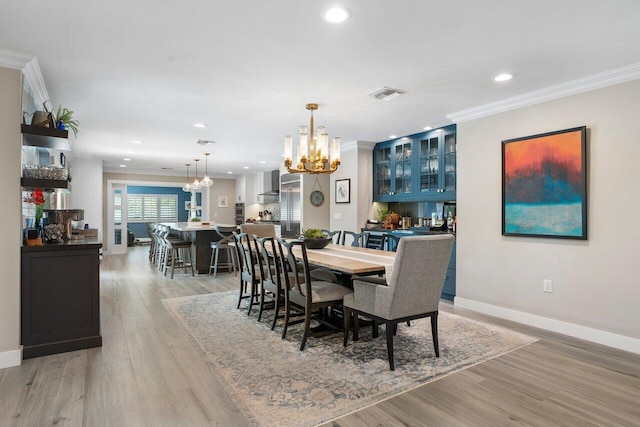 dining space with a notable chandelier, indoor bar, ornamental molding, and light hardwood / wood-style flooring